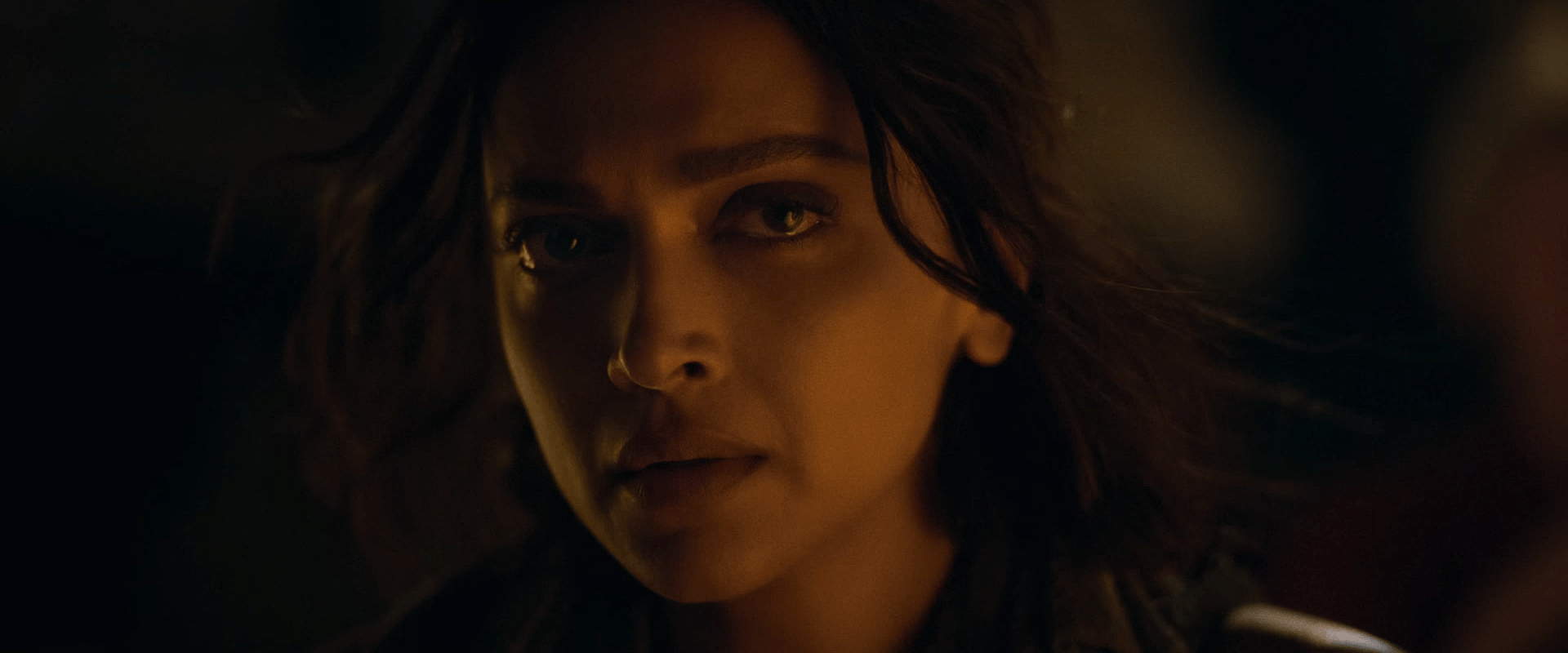 A woman lit by warm, low light stares ahead with a tense, serious expression.