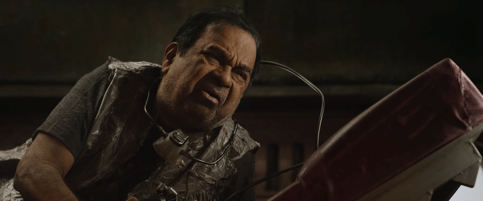 An older man wearing makeshift metallic gear lies on the ground, looking confused and distressed.