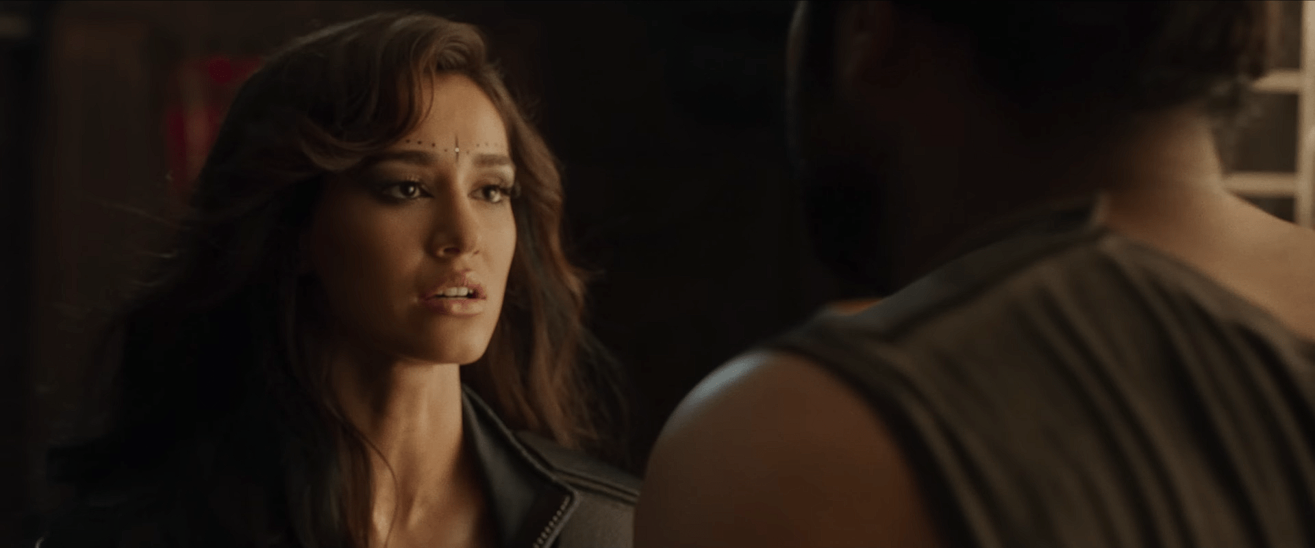 A woman with futuristic facial markings looks at someone in front of her with a worried and emotional expression.