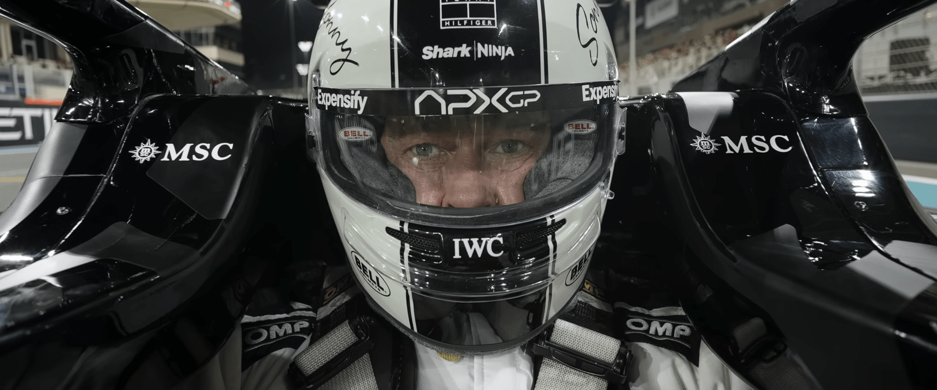 Close-up shot of Brad Pitt inside the cockpit, wearing his racing helmet and focusing on the upcoming turn in the F1 trailer.