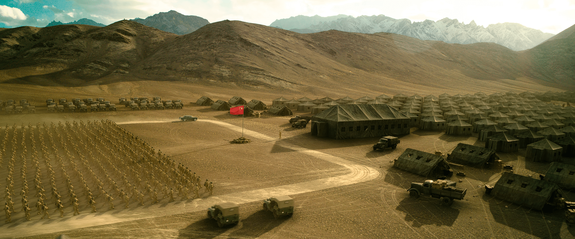 Wide shot of a massive Chinese military base with rows of marching troops, tents, trucks, and a raised Chinese flag surrounded by mountainous terrain.