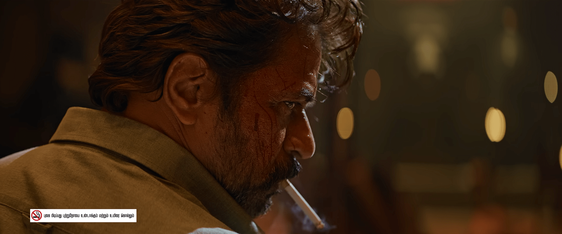 A close side profile of a man with blood on his face, holding a cigarette between his lips, standing in a warm, dim setting with blurred lights behind him.