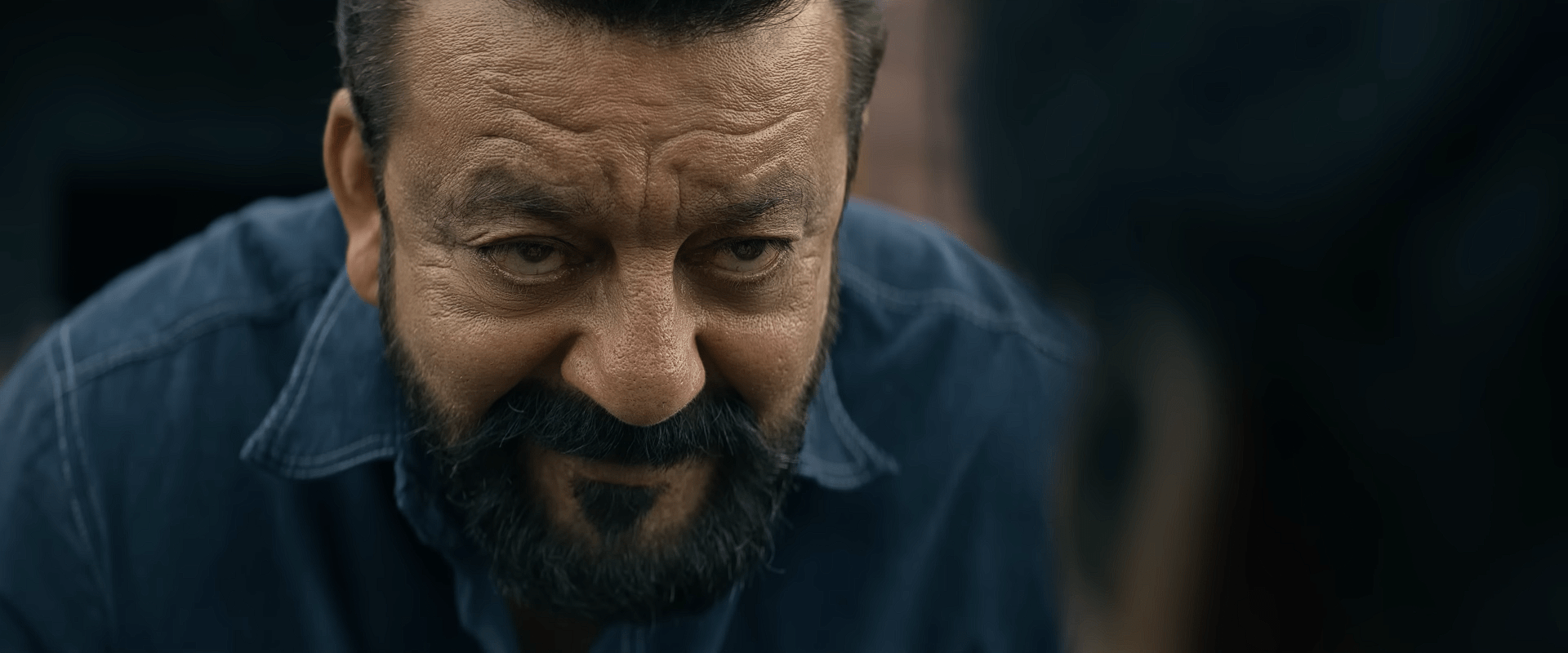 A middle-aged man with a rugged beard leans forward slightly, giving a stern, focused look, with soft daylight illuminating his face.